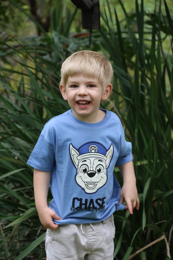 A laughing blond boy in a blue T-shirt in the garden