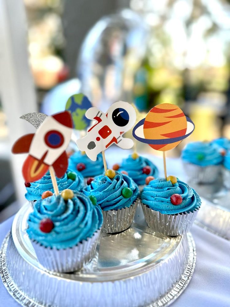 Blue-iced birthday cupcakes with rocket, astronaut and planet toppers