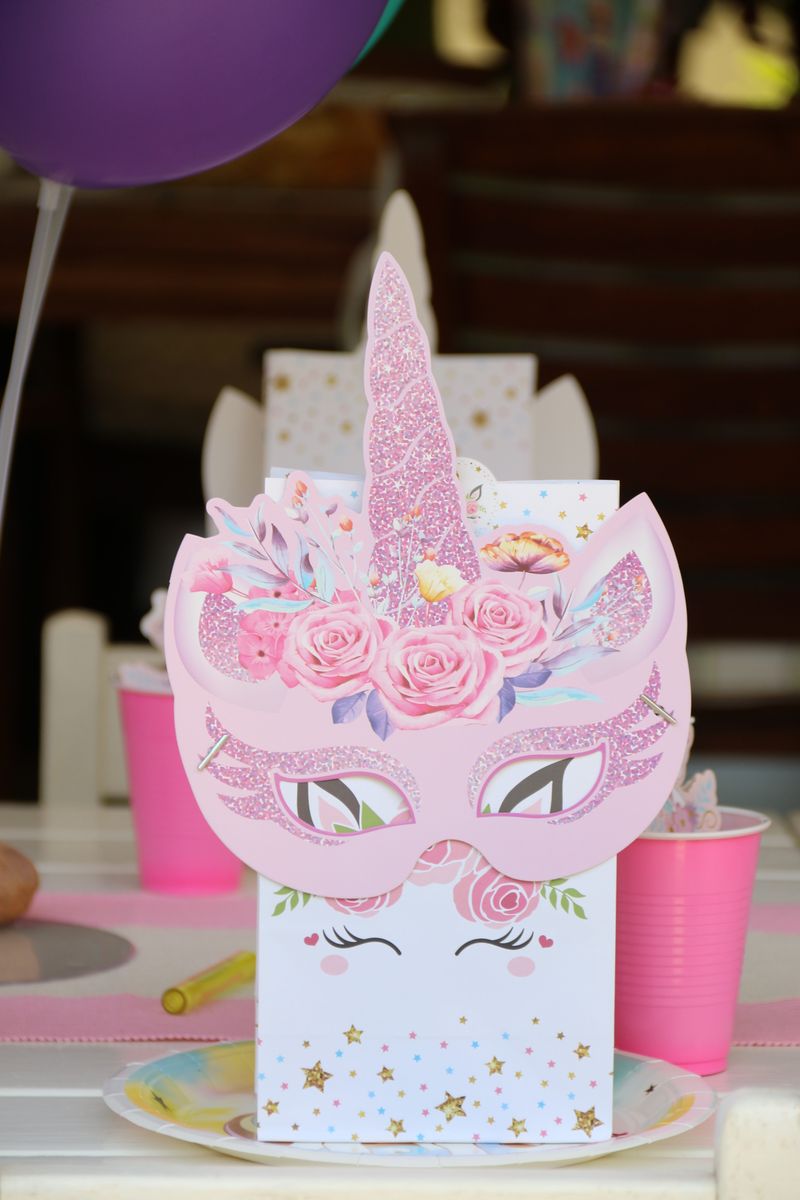A pink glittery unicorn-mask party favour bag on a pastel party table with balloons