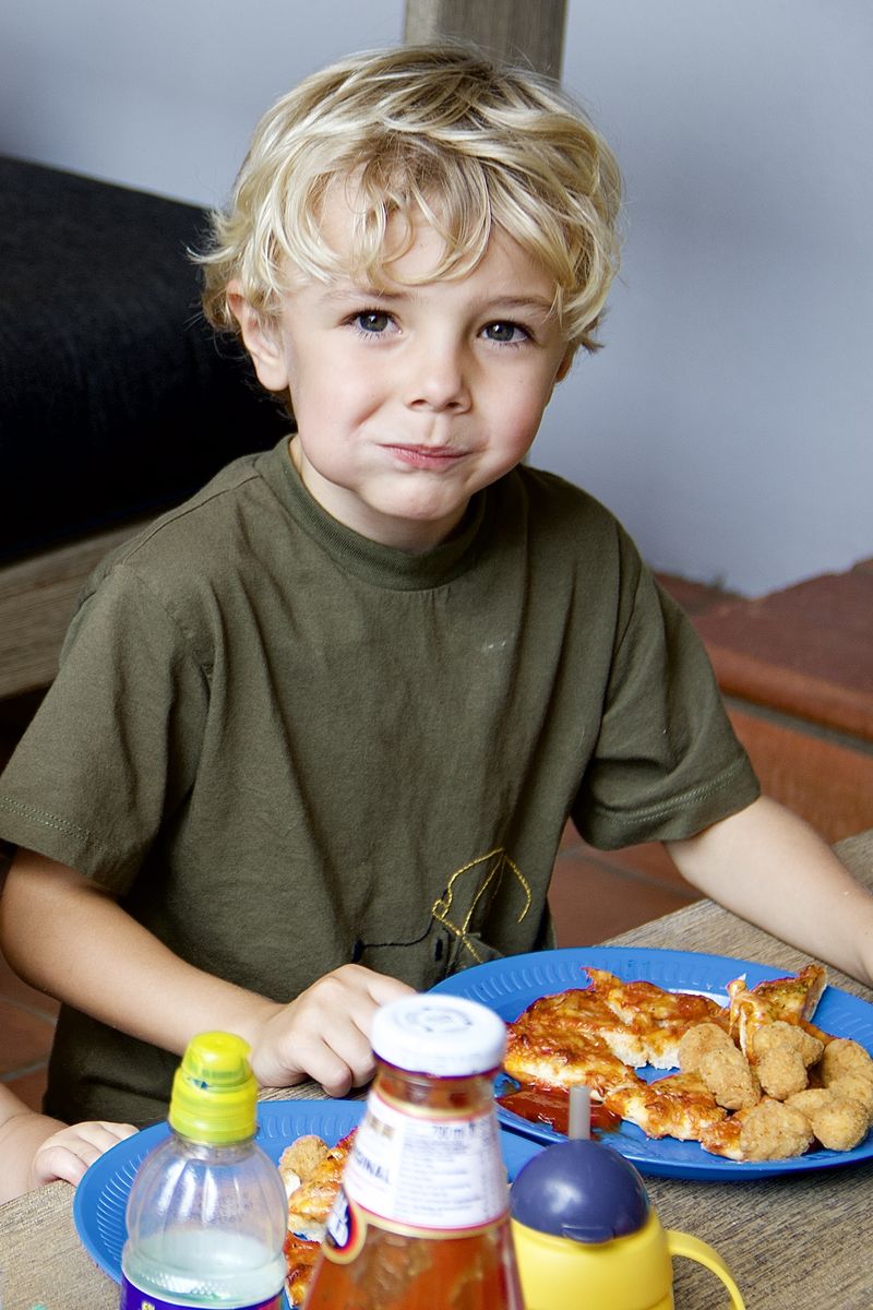 A blond boy at a party table with pizza and nuggets on a blue plate