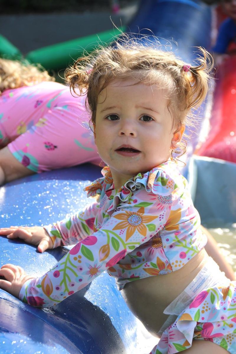 A toddler in a floral swimsuit climbing on a wet inflatable slide
