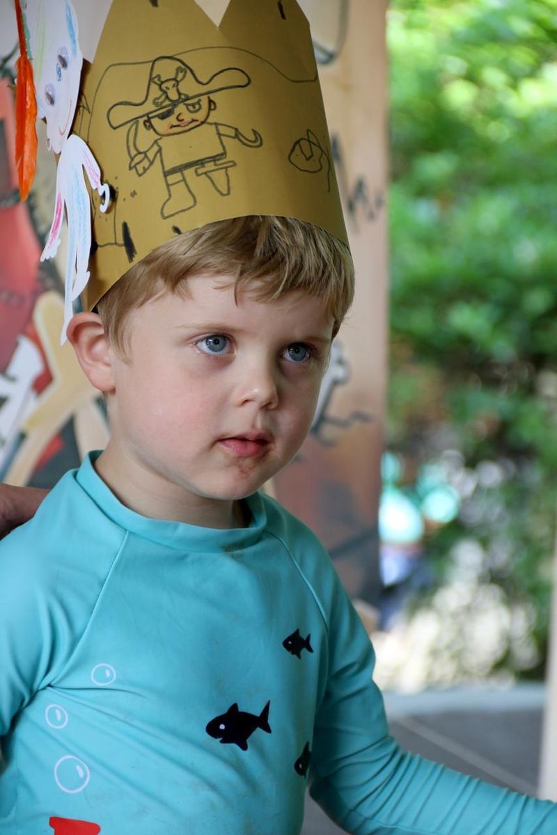 A boy in a hand-drawn pirate crown and a turquoise swim shirt