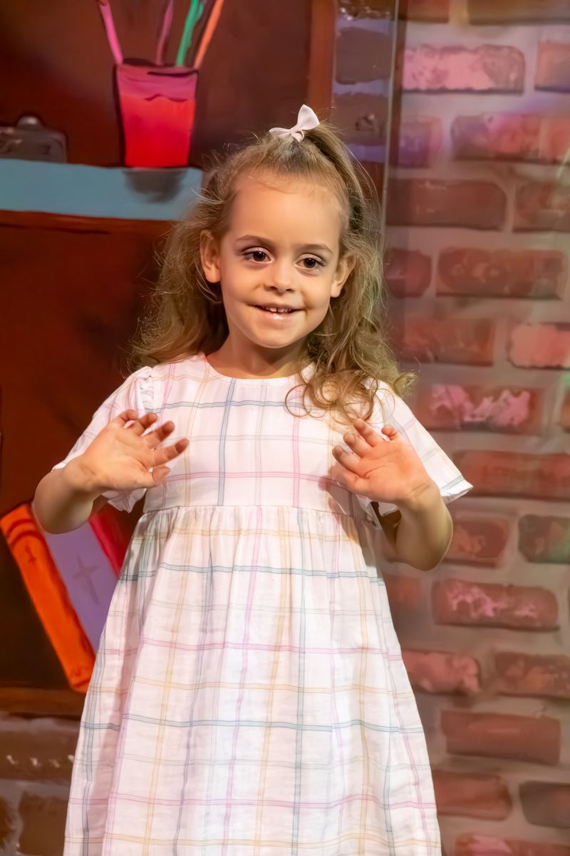 A smiling girl in a pastel check dress waving from the stage
